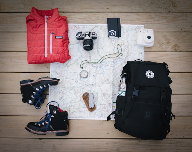 Hiking gear including, map, boots, red vest, camera and a backpack